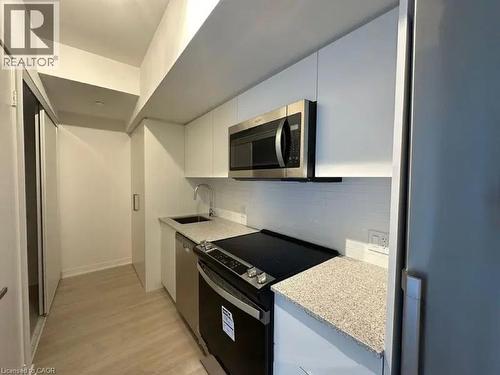 Compact kitchen featuring light wood-finish flooring, white flat-panel cabinetry, a stainless steel microwave, a range with a black cooktop, and speckled countertops - 500 Wilson Avenue Unit# 614, Toronto, ON - Indoor Photo Showing Kitchen