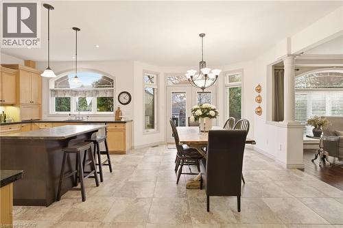 Spacious kitchen and dining area featuring stone tile flooring, light wood cabinetry, a dark kitchen island with countertop seating, and a bay window dining area with a multi-light chandelier - 129 Magnificent Way, Binbrook, ON - Indoor Photo Showing Dining Room