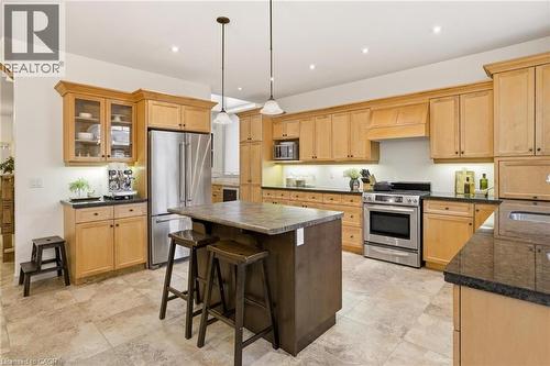 Spacious kitchen featuring extensive light wood cabinetry, stone-finish countertops, stainless steel appliances, a central island with countertop seating, and large-format floor tiling - 129 Magnificent Way, Binbrook, ON - Indoor Photo Showing Kitchen