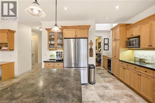 Spacious kitchen featuring extensive wood cabinetry, dark countertops, tile flooring, a stainless steel refrigerator, and integrated pendant lighting - 129 Magnificent Way, Binbrook, ON - Indoor Photo Showing Kitchen