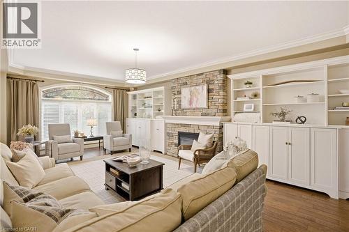 Spacious living area featuring hardwood flooring, a stone-faced fireplace with a white mantel, and extensive built-in white cabinetry and shelving - 129 Magnificent Way, Binbrook, ON - Indoor Photo Showing Living Room With Fireplace