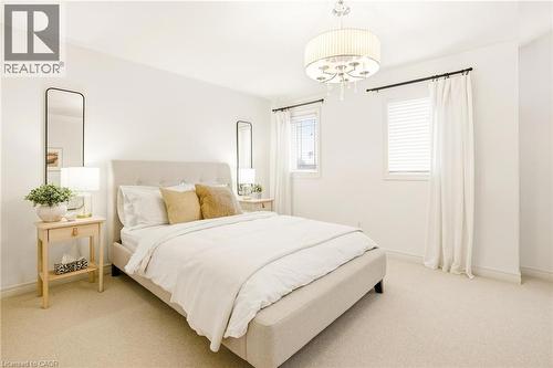 Carpeted bedroom featuring multiple windows with blinds and curtains, a drum chandelier, and a neutral color palette - 129 Magnificent Way, Binbrook, ON - Indoor Photo Showing Bedroom
