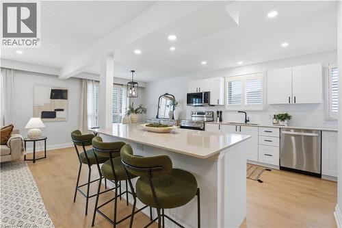 Open concept kitchen featuring a large island with a light-toned countertop, white shaker-style cabinetry, and stainless steel appliances - 11 Marcella Crescent, Hamilton, ON - Indoor Photo Showing Kitchen With Stainless Steel Kitchen With Upgraded Kitchen