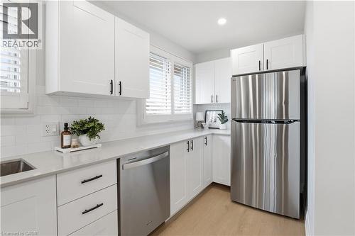 Kitchen featuring white shaker cabinetry, stainless steel appliances, a subway tile backsplash, light-toned countertops, and wood-finish flooring - 11 Marcella Crescent, Hamilton, ON - Indoor Photo Showing Kitchen With Stainless Steel Kitchen