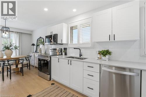 Modern kitchen featuring white shaker cabinetry, stainless steel appliances, light-toned wood-finish flooring, white subway tile backsplash, and light-toned countertops - 11 Marcella Crescent, Hamilton, ON - Indoor Photo Showing Kitchen With Stainless Steel Kitchen With Double Sink