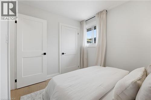 Light-filled room featuring a double-pane window with natural light, two solid panel doors with matte black hardware, and wood-finish flooring - 11 Marcella Crescent, Hamilton, ON - Indoor Photo Showing Bedroom