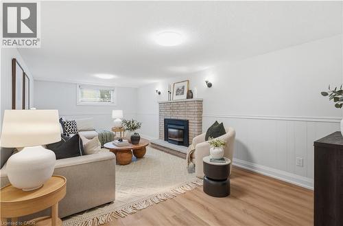 Living area featuring a brick fireplace with a black insert, wood-finish flooring, white paneled wainscoting, and recessed lighting - 11 Marcella Crescent, Hamilton, ON - Indoor Photo Showing Living Room With Fireplace