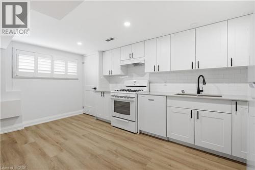 Modern kitchen featuring white shaker-style cabinetry with matte black hardware, a white subway tile backsplash, and light-toned wood-finish flooring - 11 Marcella Crescent, Hamilton, ON - Indoor Photo Showing Kitchen