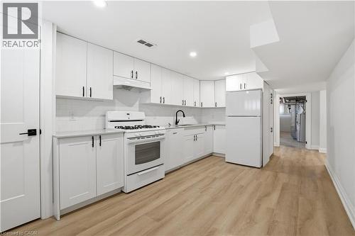 Kitchen featuring white cabinetry, subway tile backsplash, light wood-finish flooring, white appliances, and matte black hardware - 11 Marcella Crescent, Hamilton, ON - Indoor Photo Showing Kitchen