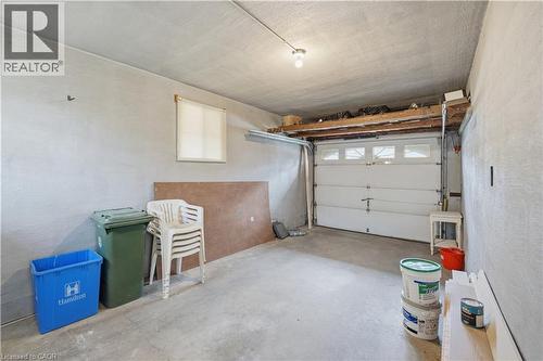Attached single-car garage featuring a concrete floor, overhead garage door with upper window panels, and a single window with blinds - 11 Marcella Crescent, Hamilton, ON - Indoor Photo Showing Garage