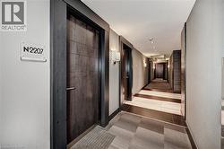 Entryway featuring a dark wood-finish door with modern hardware, sconce lighting, and a patterned carpet runner - 