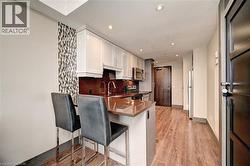 Contemporary kitchen featuring white shaker-style cabinetry, a rich brown countertop, stainless steel appliances, and wood-finish flooring - 