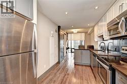 Contemporary kitchen featuring stainless steel appliances, wood-finish flooring, recessed lighting, white cabinetry, and dark countertops - 