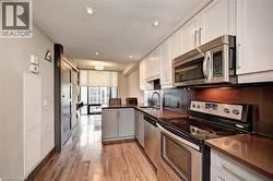 Modern kitchen featuring stainless steel appliances, light-toned upper cabinetry, contrasting lower cabinetry, and a dark-toned countertop - 