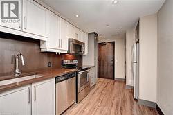 Modern kitchen featuring white cabinetry, stainless steel appliances, a brown countertop, coordinating backsplash, and wood-finish flooring - 