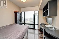Bedroom featuring expansive floor-to-ceiling windows, wood-finish flooring, a built-in desk with integrated shelving, and a dark wood cabinet - 