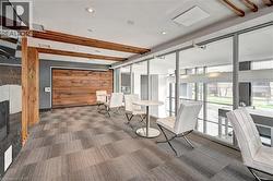 Interior space featuring floor-to-ceiling windows, wood-finish accent wall, ceiling-mounted wood beams, recessed lighting, and patterned carpet flooring - 