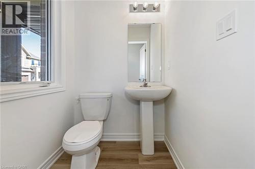 Pedestal sink with mirror and vanity lighting, white toilet, wood-finish flooring, and a window with white trim - 205 Thames Way Unit# 31, Hamilton, ON - Indoor Photo Showing Bathroom