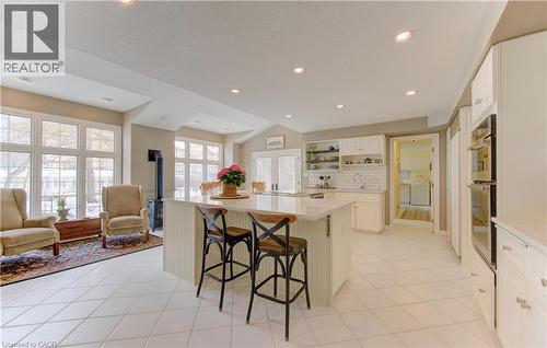 Spacious kitchen featuring an expansive central island with seating, white cabinetry, integrated double wall ovens, and white tile flooring - 514 Colonial Drive, Waterloo, ON - Indoor