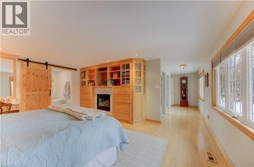 Built-in wood cabinetry with a central fireplace, multiple windows with natural wood trim, light wood-finish flooring, and a sliding barn door - 514 Colonial Drive, Waterloo, ON - Indoor Photo Showing Bedroom