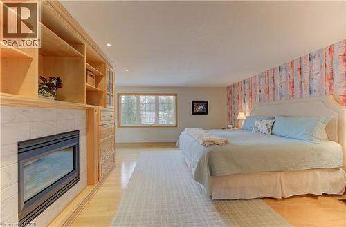 Light wood-finish flooring complements a built-in entertainment center featuring open shelving, glass-front cabinetry, and an integrated fireplace with a tiled surround - 514 Colonial Drive, Waterloo, ON - Indoor Photo Showing Bedroom With Fireplace