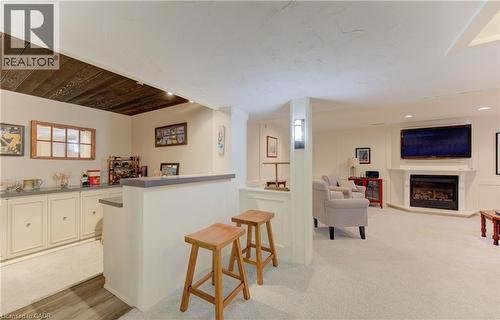 Finished lower level featuring a built-in wet bar with cabinetry, wood-finish flooring, a wall-mounted fireplace, and recessed lighting - 514 Colonial Drive, Waterloo, ON - Indoor Photo Showing Other Room With Fireplace