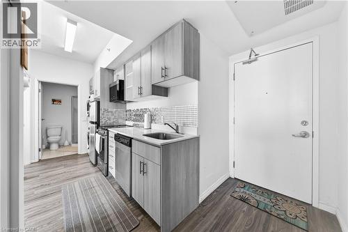 Compact kitchen featuring wood-finish flooring, light-toned cabinetry with dark hardware, stainless steel appliances, a mosaic tile backsplash, and a single basin sink - 246 Lester Street Unit# Ph-03, Waterloo, ON - Indoor Photo Showing Kitchen
