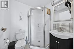 Compact bathroom featuring a corner shower with glass enclosure, white toilet, and a vanity with a dark cabinet and integrated sink - 
