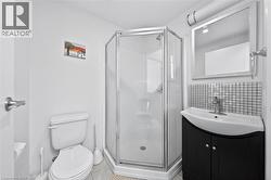Compact bathroom featuring a corner shower enclosure with clear glass, a black vanity with an integrated sink, a tiled backsplash, and a wall-mounted mirror with overhead lighting - 