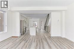 Open-concept interior featuring light wood-finish flooring, white walls, and a modern kitchen with stainless steel appliances - 