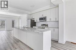 Modern kitchen featuring a large island with a double stainless steel sink, white flat-panel cabinetry, stainless steel appliances, white subway tile backsplash, and wood-finish flooring - 