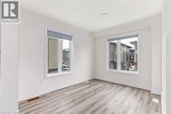 Light-filled interior space featuring wood-finish flooring, white walls, two large windows with roller shades, recessed ceiling lighting, and crisp white baseboards - 