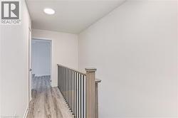Hallway featuring wood-finish flooring, a contemporary railing with black balusters, and a recessed ceiling light - 