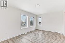 Spacious room featuring light wood-finish flooring, white walls, and a contemporary ceiling light fixture - 