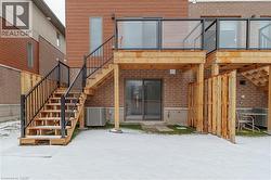 Rear exterior featuring a wood-plank deck with glass panel railings, accessible via a wood staircase with black metal railings - 