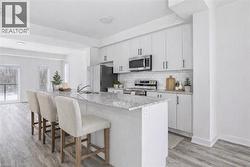 Modern kitchen featuring white cabinetry, stainless steel appliances, a subway tile backsplash, and a large island with a light-toned granite countertop - 