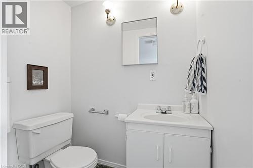 White vanity with an integrated sink and base cabinetry, featuring a wall-mounted mirror, two sconce light fixtures, and a white toilet - 137 Market Street, Hamilton, ON - Indoor Photo Showing Bathroom