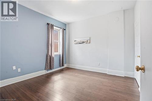 Room featuring wood-finish flooring, a window with drapery, a light blue accent wall, and white trim - 137 Market Street, Hamilton, ON - Indoor Photo Showing Other Room
