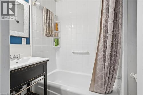 Bathroom featuring a white subway tile tub surround, white bathtub, distressed black vanity with white basin sink, and a framed mirror - 137 Market Street, Hamilton, ON - Indoor Photo Showing Bathroom