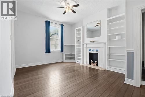 Living area featuring wood-finish flooring, a decorative fireplace with mantel, built-in shelving, a ceiling fan, and a window with natural light - 137 Market Street, Hamilton, ON - Indoor With Fireplace