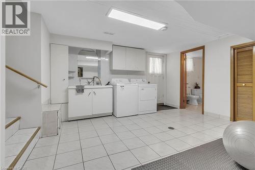 Tiled flooring throughout a utility space featuring a laundry area with built-in cabinetry, a utility sink, and a washer and dryer - 2344 Brinell Avenue, Burlington, ON - Indoor Photo Showing Laundry Room