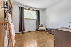 Room featuring wood-finish flooring, a window with natural wood trim, and white painted walls - 