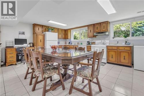 Open-concept kitchen and dining area featuring light-toned tile flooring, light wood cabinetry, white appliances, and multiple windows - 2344 Brinell Avenue, Burlington, ON - Indoor