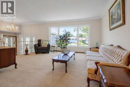 Spacious living area featuring expansive windows, neutral carpeting, crown molding, and a crystal chandelier - 2344 Brinell Avenue, Burlington, ON - Indoor Photo Showing Living Room