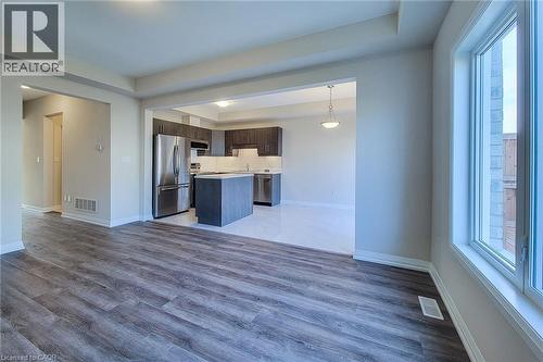 Open-concept living area with wood-finish flooring, leading to a kitchen featuring an island, stainless steel appliances, and dark wood cabinetry - 111 Alicia Crescent, Thorold, ON 