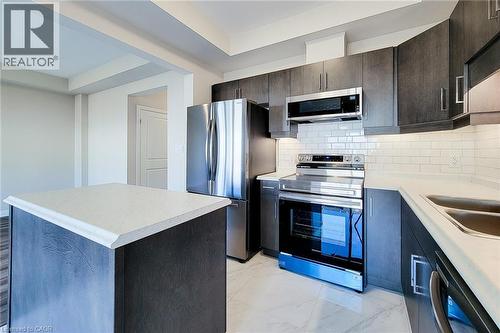 Modern kitchen featuring an island, full-height dark wood-finish cabinetry, stainless steel appliances, white subway tile backsplash, and light-toned countertops - 111 Alicia Crescent, Thorold, ON 