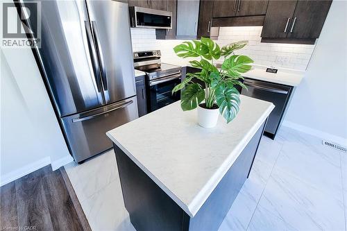 Contemporary kitchen featuring a central island with a light-toned countertop, dark wood-finish cabinetry, stainless steel appliances, white subway tile backsplash, and mixed flooring of wood-finish a - 111 Alicia Crescent, Thorold, ON 