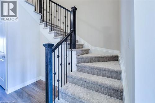 Carpeted staircase featuring black wrought iron balusters and a dark wood newel post - 111 Alicia Crescent, Thorold, ON 