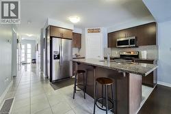Contemporary kitchen featuring a peninsula with a stone countertop, dark wood-finish cabinetry, stainless steel appliances, and a tiled backsplash - 