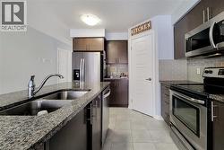 Kitchen featuring dark wood cabinetry, stainless steel appliances, granite countertops, a double basin sink with a high-arc faucet, and light grey subway tile backsplash - 